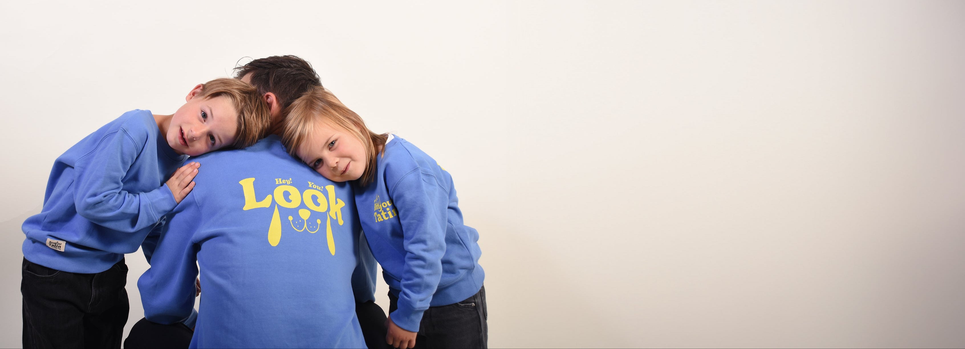 Two children wearing blue sweatshirts with a logo on a plain background
