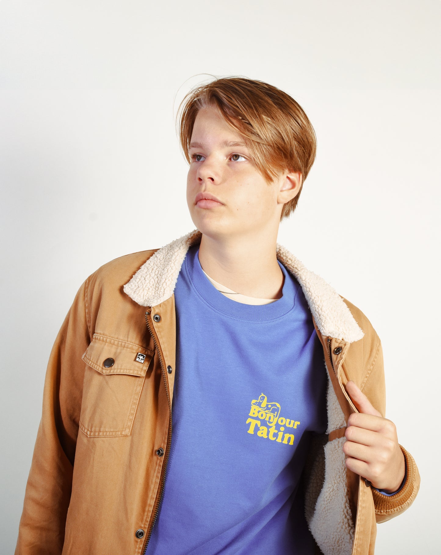 Person wearing a brown jacket and blue t-shirt with a logo on a white background